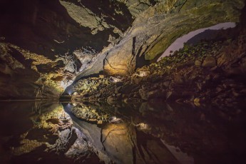Hang En Cave: Im See vor dem gewaltigen Boulderhaufen spiegeln sich drei Lichter, in dessen Schein man unsere drei Beleuchter als schwarze Umrisse erkennen kann.