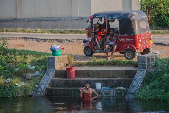 Washday in Polonnaruwa: Mama is having a bath and is brushing her teeth while papa and son are watching the scene and wishing everyone "a nice day".