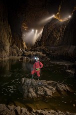 Wie ein Bergsteiger in den Alpen der Unterwelt steht Guide Borut Lozej auf einem Felsen im unterirdischen Reka-Fluss. Weiter oben illuminieren Lichter auf den Besucherwegen die größte unterirdische Schlucht Europas.
