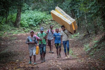 With heavy cargo on their heads, young men trek through the dense rainforests of the Amber Mountains.