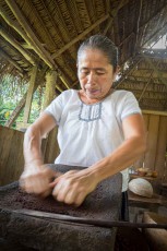 Anita Cals Hände treiben den Mahlstein über geröstete Kakaobohnen – unter dem Palmstrohdach der Living Maya Experience in Toledo.