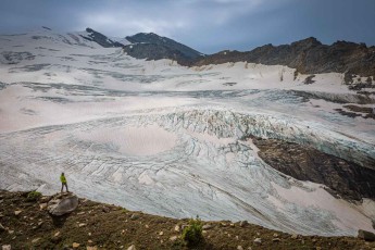 Guide Fridjon stands on a boulder – looking tiny against the white and pink-speckled ice of the South Canoe Glacier’s terminus, which flows out of the mountains like a frozen river.