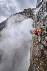A battle of the elements: a waterfall of meltwater lashing against the granite flanks in white plumes. We press our hands and feet against the steel of the via ferrata.