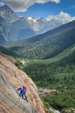 I brace myself against the reddish-patterned granite of the Zillmer Canyon Via Ferrata. Below me, the Cariboo Valley opens out into endless coniferous forests, with glaciers on snow-white peaks beyond (photo by Jennifer Malloy).
