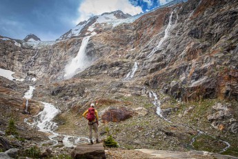 Jennifer Malloy gazes in wonder at the vast cirque below Mount Zillmer. Several waterfalls plunge down the reddish-brown, veined rock face and feed a young stream that winds its way through the scree.