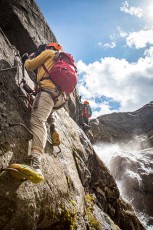 Two climbers work their way through Zillmer Canyon, clipped to the iron path of the via ferrata. Beside them, white water hammers wet stone.