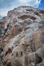 Three climbers inch their way up the granite-grey face of Zillmer Canyon, their orange and red harnesses bright against ochre-streaked rock.