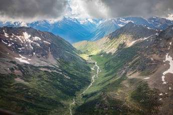 Silver meltwater winds through a jade-green valley floor, flanked by anthracite ridges still carrying white patches of late snow.