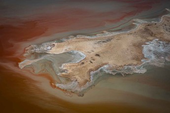 Karminrot leuchtet das Wasser des Lake Eyre, wo sich Salzkristalle und Sedimente zu organischen Mustern formen. Sandinseln treiben wie verwitterte Knochen in der flüssigen Wüste. Mineralien färben die Ufer rostrot und ascheblau.