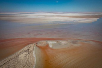 Salzkrusten zeichnen Spiralen in das fast ausgetrocknete Seebett. Windströmungen haben die Sedimente zu geometrischen Mustern verdichtet. Der Horizont verschmilzt mit dem Himmel zu einer Linie, die jede Orientierung auflöst.