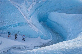 Drei Gestalten auf einem Schneegrat zwischen den Wänden einer Eisschlucht – erst aus der Luft wird sichtbar, wie tief das Schmelzwasser sich in die Eiskappe geschnitten hat.
