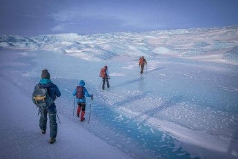 Die Gruppe quert einen zugefrorenen Schmelzwassersee – im Sommer sucht sich das Wasser hier Schächte durch das Eis, Mühlen genannt, die im Winter unter Schnee verschwinden.