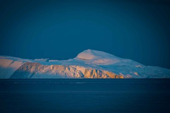 Illulisat: Warmes Licht streift über die Eiskante, als würde die aufgehende Sonne nach der Felswand greifen.