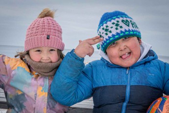 Oqaatsut: Zwei Kinder salutieren auf einer Bank des Dorfplatzes.