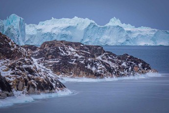 Hinter der schwarzen Felsküste staut sich das Eis des Ilulissat-Eisfjords – am Fjordausgang laufen die Eisberge auf einer Endmoräne auf, manche für Jahre, bis sie dann darübergleiten.