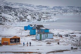 Drei Kinder spielen Fussball im Schnee Oqaatsuts. Hinter ihnen treiben Eisschollen im grauen Wasser.