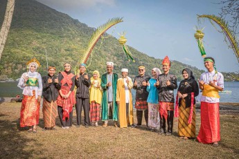 Das vollständige Empfangskomitee: dreizehn festliche Gewänder, zwei Bögen aus jungen Kokoswedeln, dahinter der 640 Meter hohe Gunung Api.