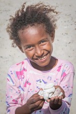 Hände voll Muscheln, am Strand aufgelesen – der weiße Sand, auf dem das Mädchen steht, ist nichts anderes als zerriebene Schale und Korallenkalk.