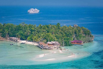 Die Insel Kri aus der Luft: ein paar Dächer im Palmenwald, davor Sandbänke, dahinter die Le Soléal.