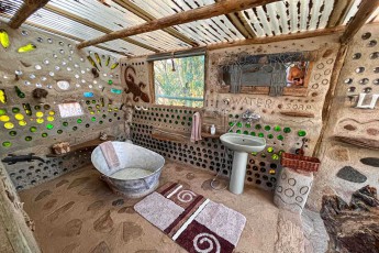 Glas statt Fenster: Im Bad des Bottle House auf der Molope Farm leuchten Flaschenböden in der Lehmwand – darunter wartet eine Zinkwanne.