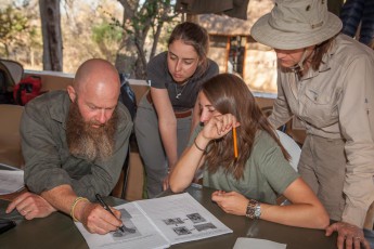 Bruce erklärt Sophie, Martina und Kim anhand von Fotos, wo sich bei verschiedenen Tieren das Gehirn befindet. Im Falle eines Angriffs muss der Schütze es mit seinem ersten Schuss treffen.