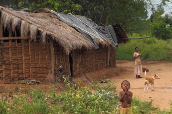 Wife, child, house, dogs and mud hut of Guna Bandiya, where i am living during my stay. A plastic tarpaulin has to serve temporarily as replacement for the dry grass, which is growing rarely in the Vedda people area.