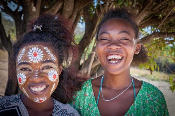 Mit ihrer kunstvoll aufgetragenen traditionellen Gesichtsbemalung aus weißen floralen Mustern strahlt die 33-jährige Mboty neben ihrer fröhlichen Tochter in der Taubenbucht - die zeremoniellen Designs mit Blüten und geometrischen Elementen sind Teil der madagassischen Kulturtradition und werden oft für besondere Anlässe oder Feste getragen.