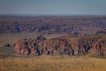 Im Vordergrund erheben sich die charakteristischen orangeroten Felstürme und -säulen der Bungle Bungles aus der grünen Ebene, während sich dahinter wellenförmige Erosionsstrukturen bis zum Horizont erstrecken.