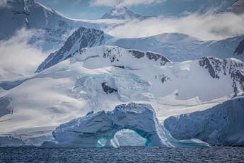 A huge ice arch frames the view of the glaciers behind it. Waves and meltwater have created this gateway – a transient work of art in front of eternal, snow-covered peaks.