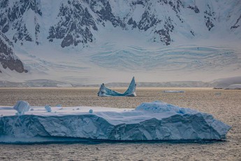Behind a table iceberg, a weathered iceberg stretches its pointed spikes like shark teeth towards the sky. The crevasses in the ice shelf tell of enormous forces – this is where the ice giants calve, later wandering through the Southern Ocean.