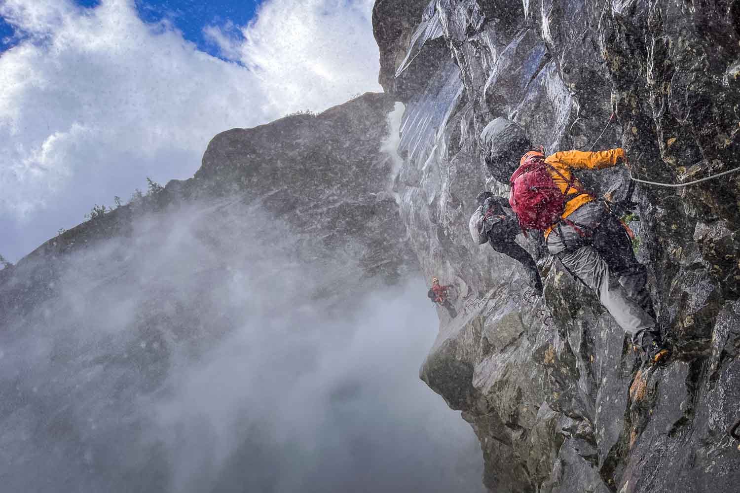 A battle of the elements: a waterfall of meltwater lashing against the granite flanks in white plumes. We press our hands and feet against the steel of the via ferrata.