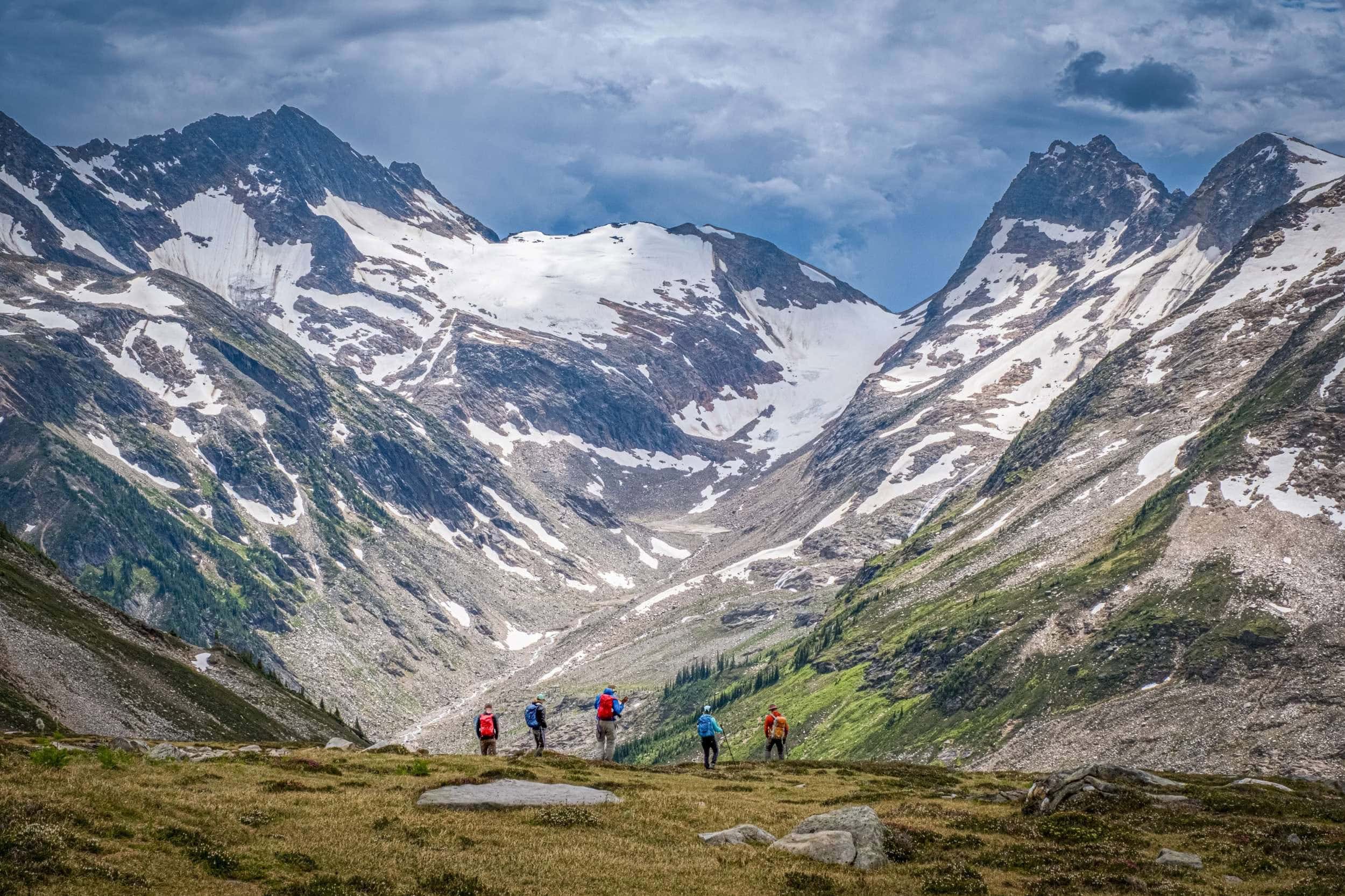 Fünf Wanderer vor dem weiten Gletscherkar der Cariboo Mountains, mit schroffen Granitflanken und Schneefeldern.
