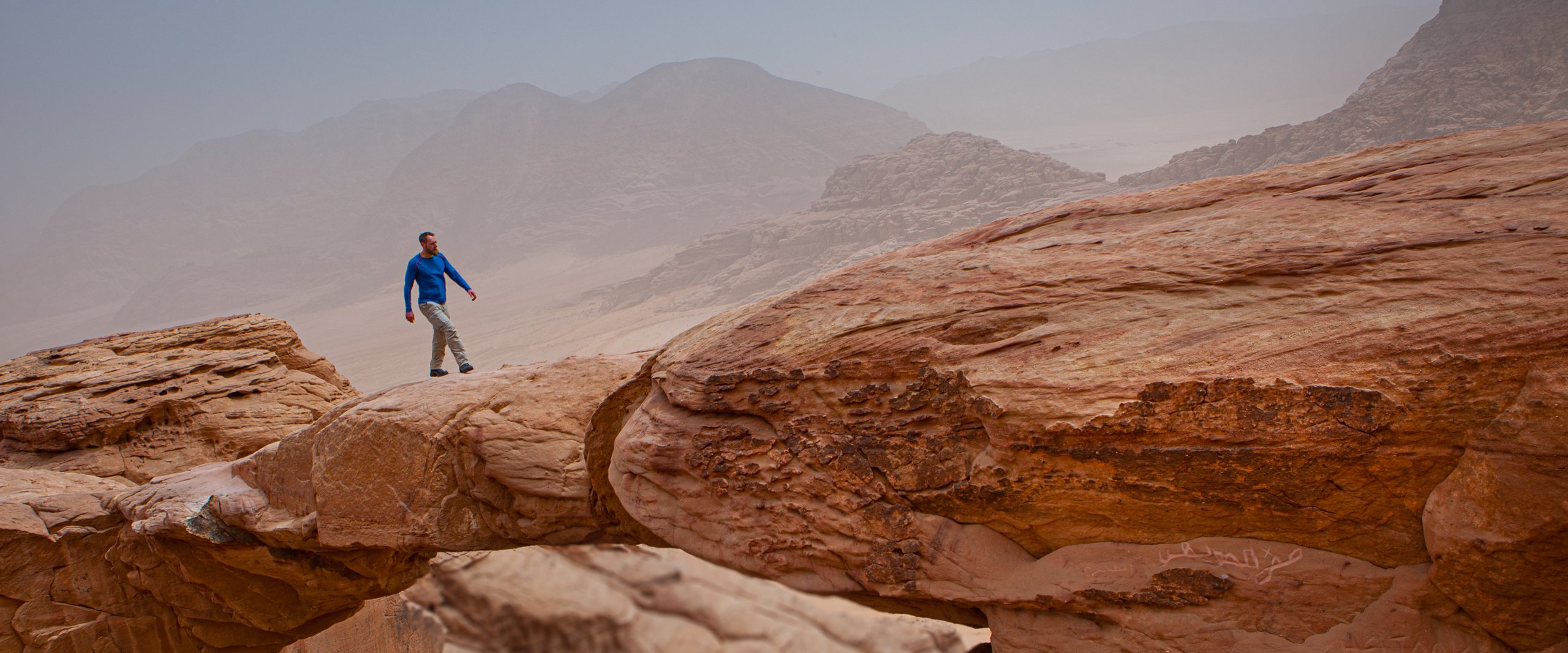 Malte Clavin läuft im Sandsturm über einen Felsbogen im Wadi Rum