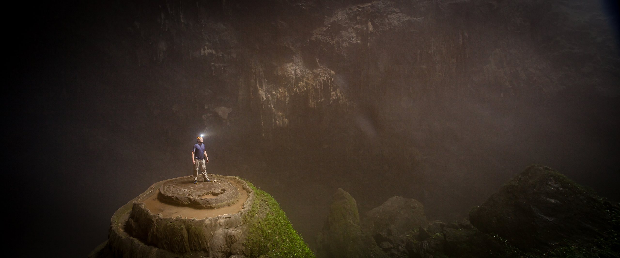 Malte Clavin steht winzig auf einem Felsdom im Nebel einer riesigen Höhle in Vietnam