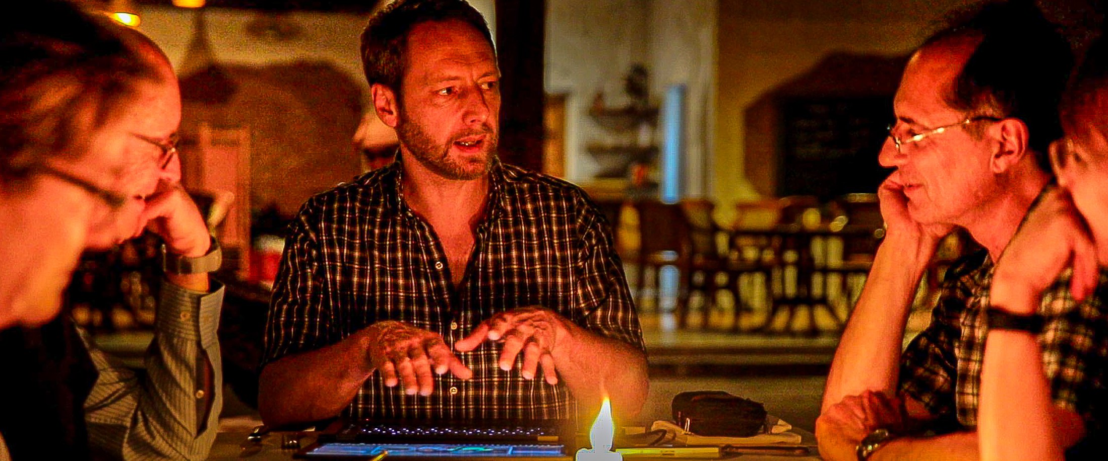 Malte Clavin erklärt abends am Tisch im Kerzenlicht, drei Gäste hören zu