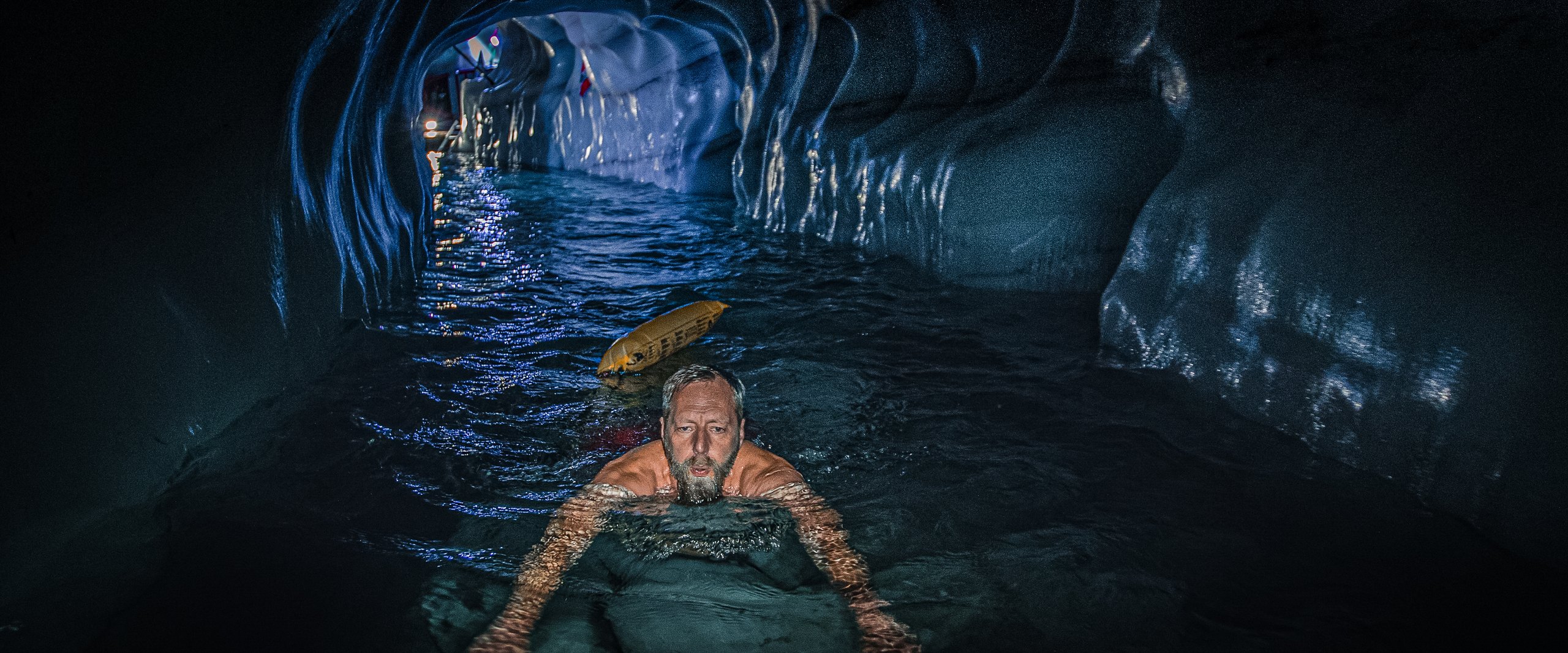 Malte Clavin schwimmt durch eine blau leuchtende Gletscherhöhle